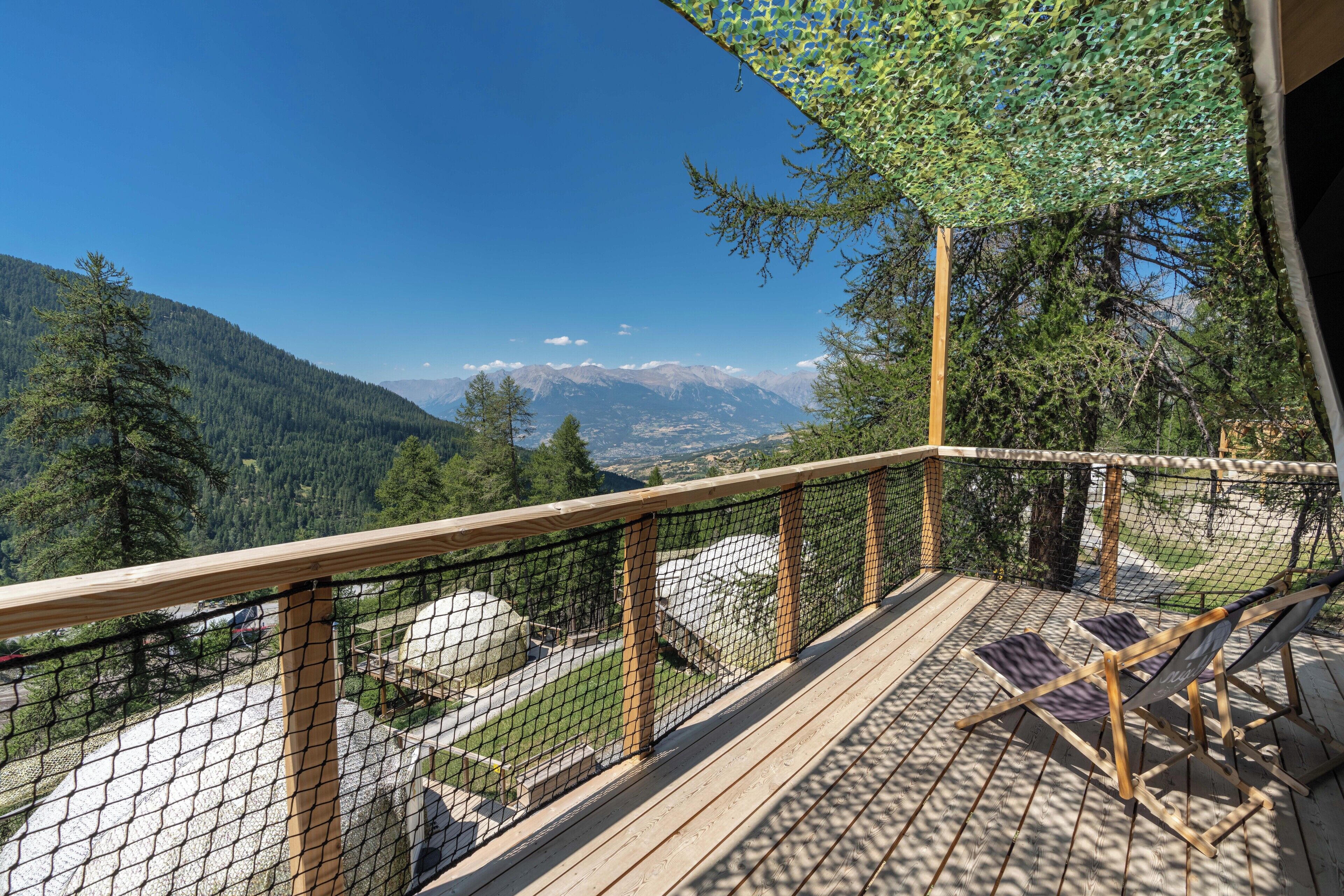 A deck with a view of mountains, a wooden railing, and a hammock.