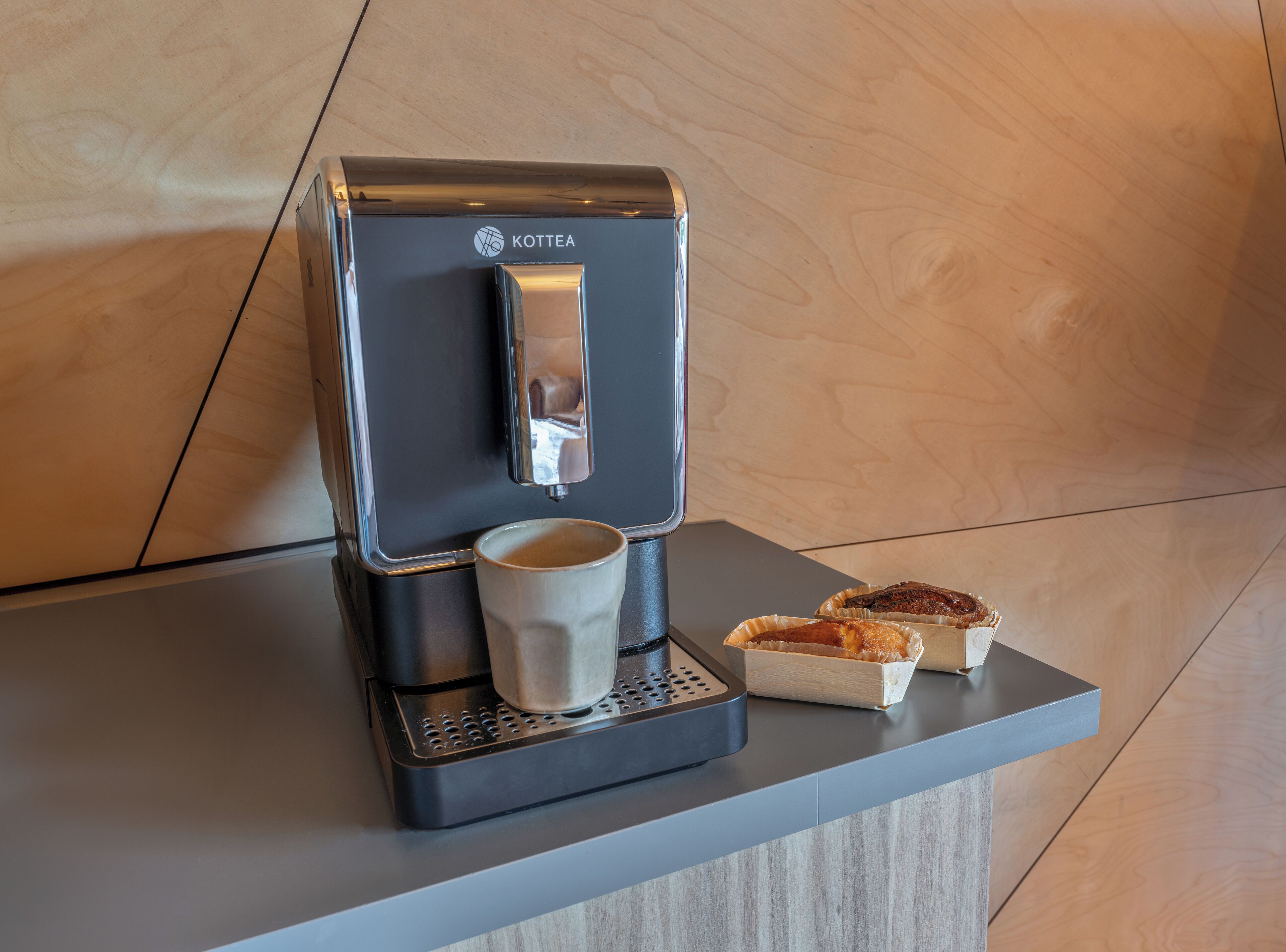 A coffee machine with a cup and two pastries on a countertop.