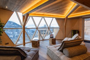 Une pièce chaleureuse avec une grande fenêtre, des poutres en bois et une vue sur des montagnes enneigées.