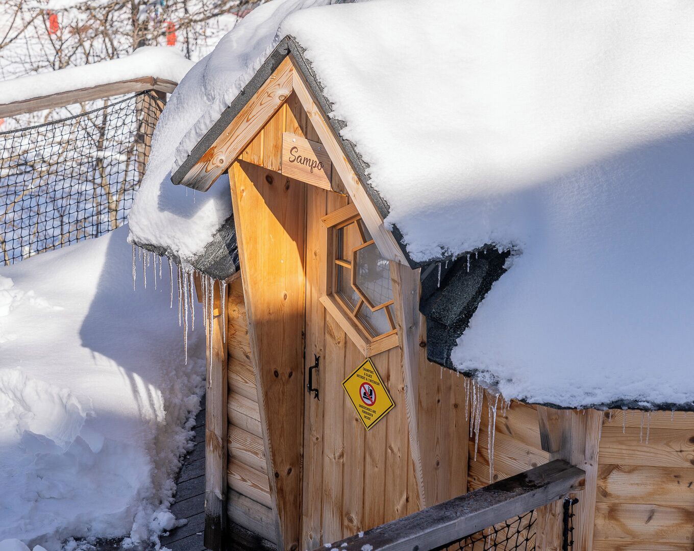 A wooden cabin with a snow-covered roof and a sign reading "Sampo."