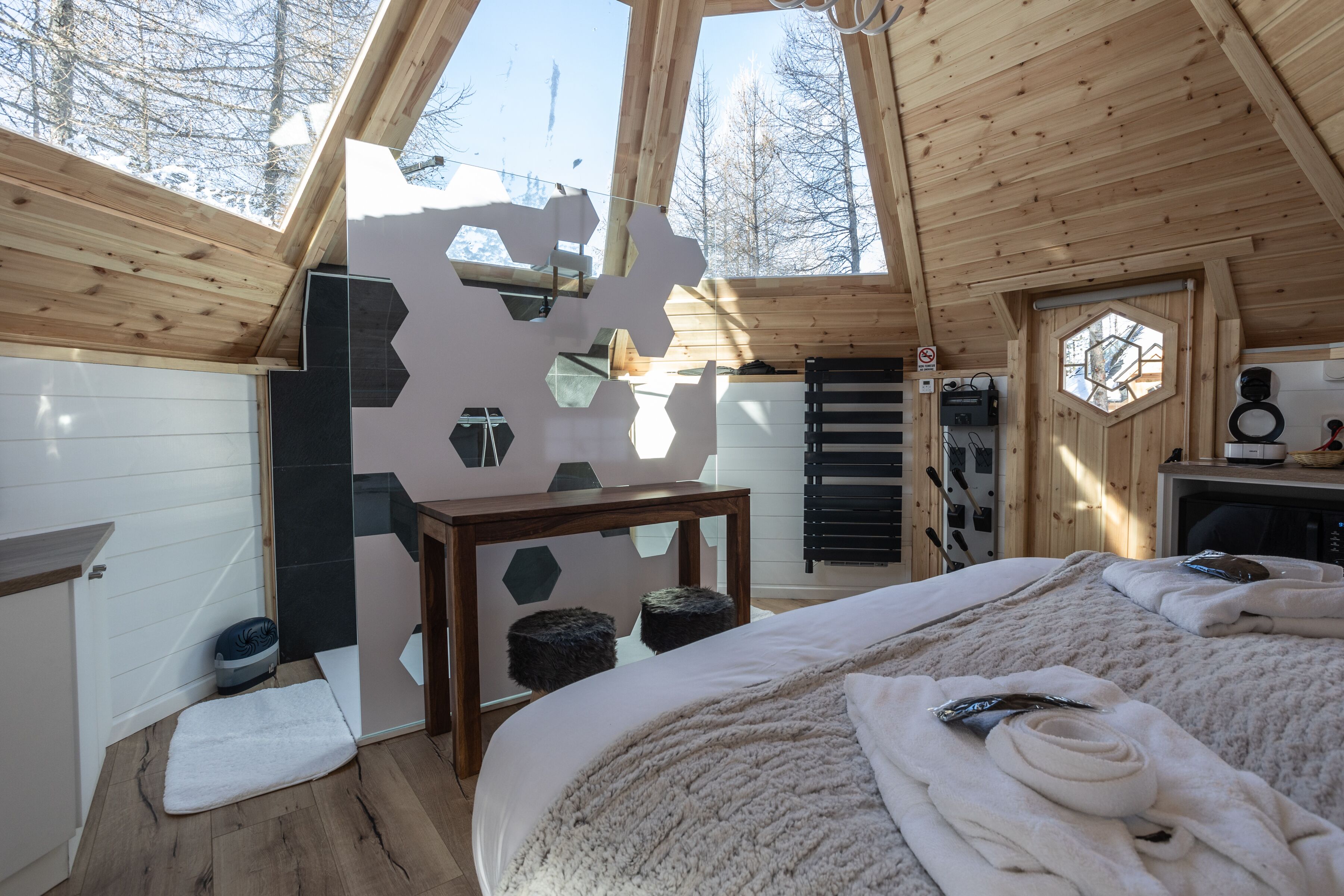 A cozy wooden cabin with a large bed, a small table, and a unique hexagonal wall design.