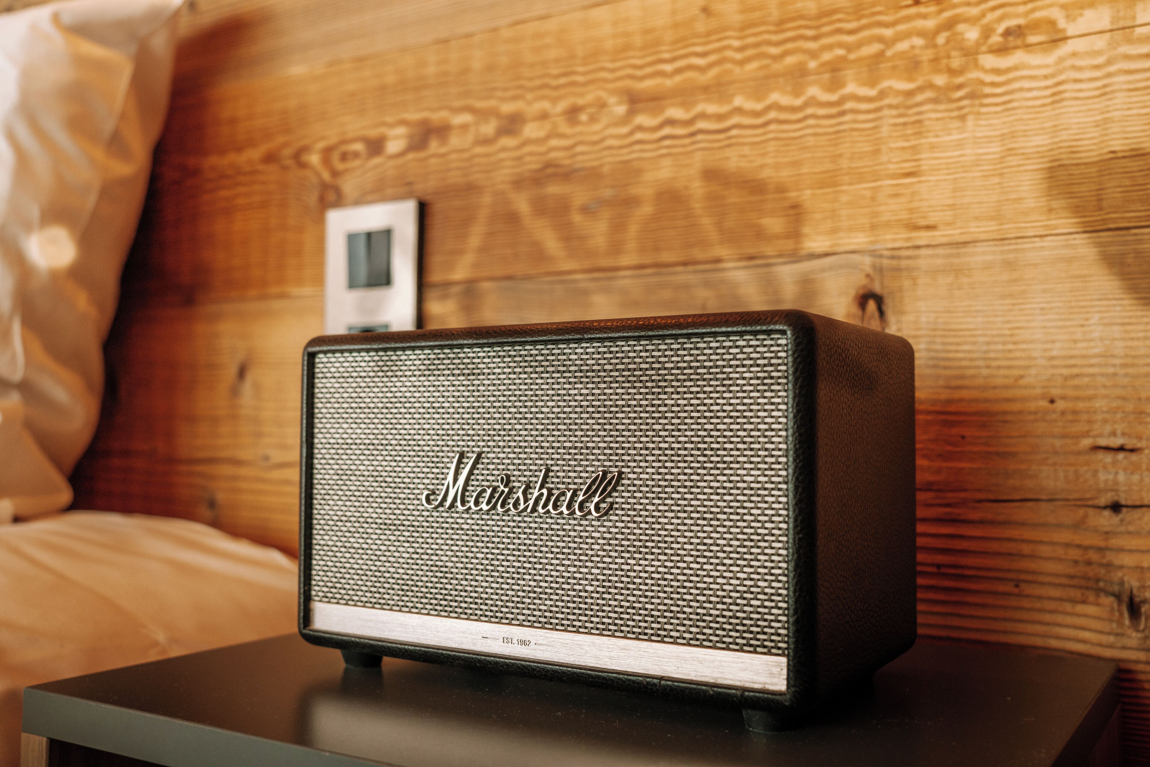 A Marshall speaker on a bedside table in a room with wooden paneling.