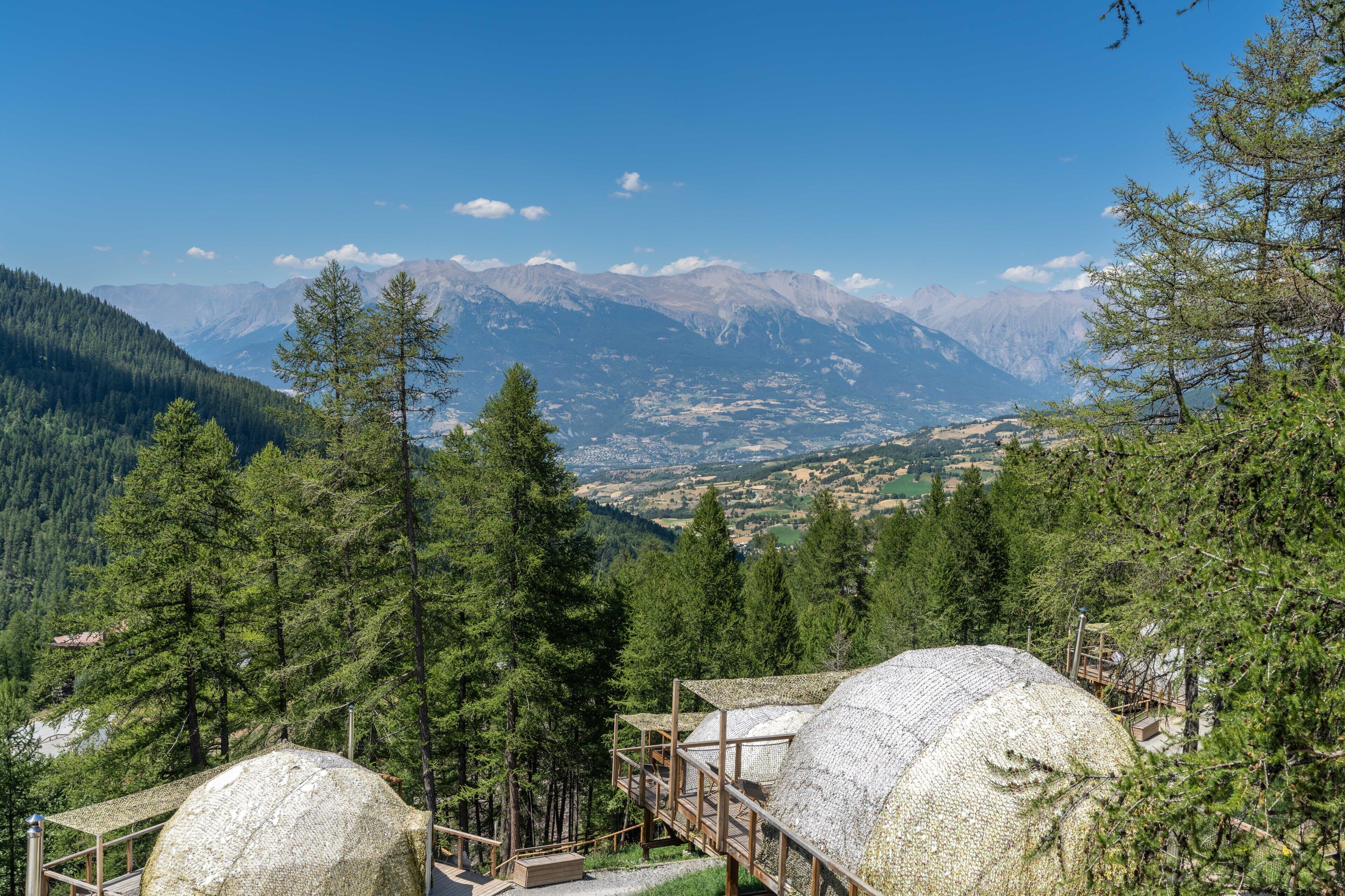 A mountain lodge with a view of snow-capped peaks, surrounded by dense forest.