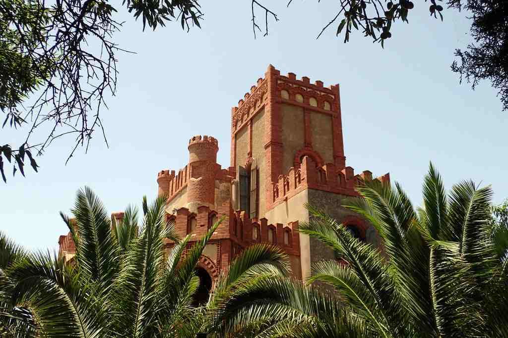 A large, historic building with a prominent tower and arched windows, surrounded by palm trees.