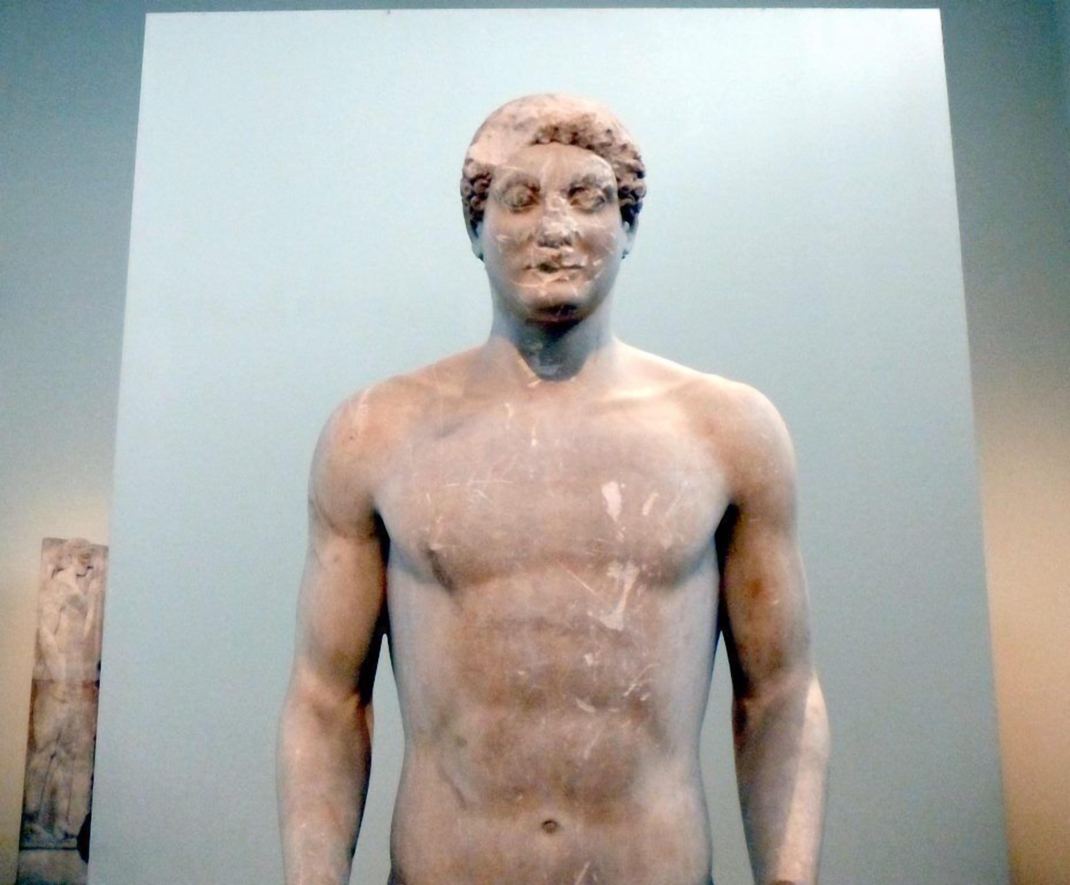 A marble statue of a male figure with a muscular build, standing against a plain background.