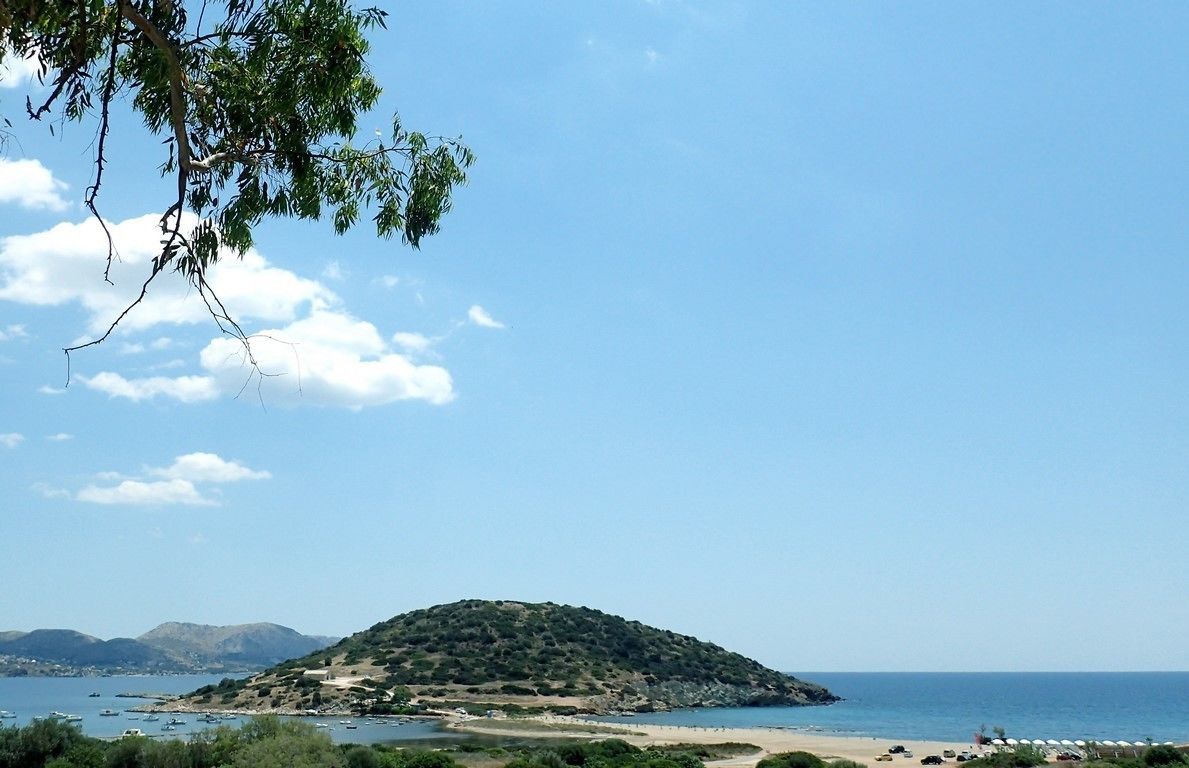 A coastal landscape with a hill, beach, and clear sky.