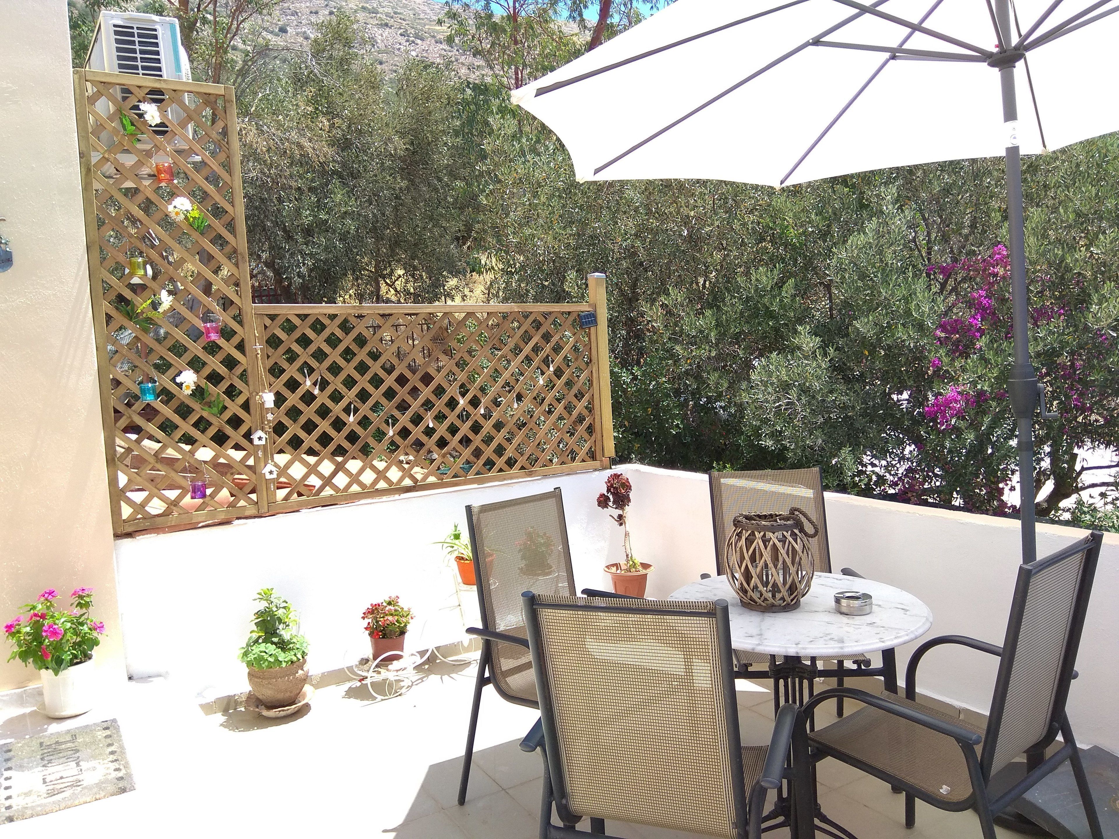An outdoor patio with a round table and chairs, surrounded by potted plants and a lattice fence.