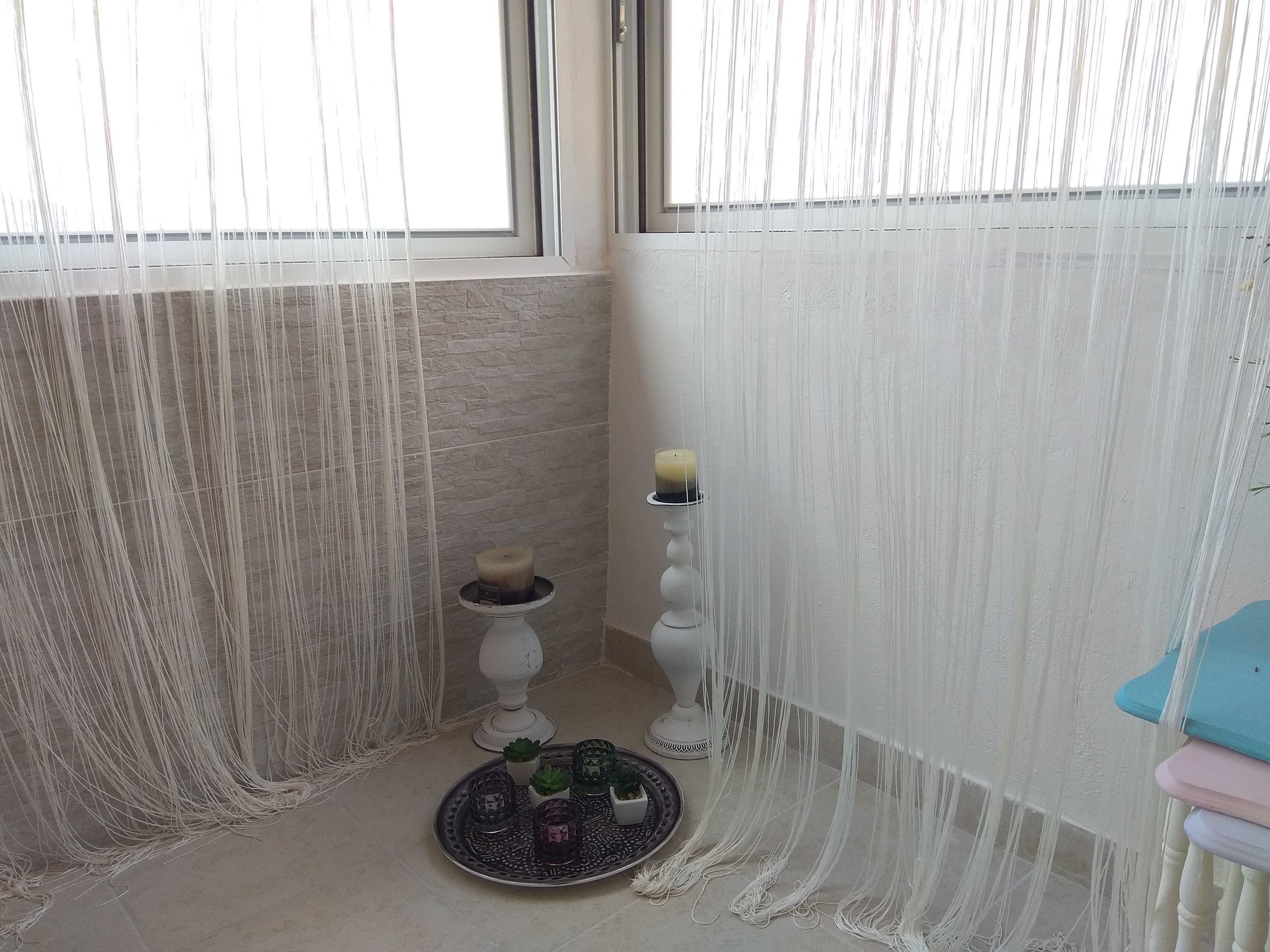A corner of a room with a window, a white curtain, a candle holder with a candle, and a tray with small plants.
