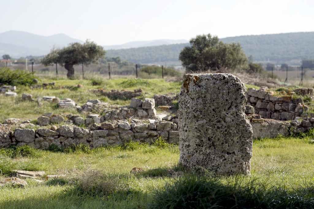 Una antigua estructura de piedra en un entorno rural, con un muro de piedra y restos dispersos al fondo.
