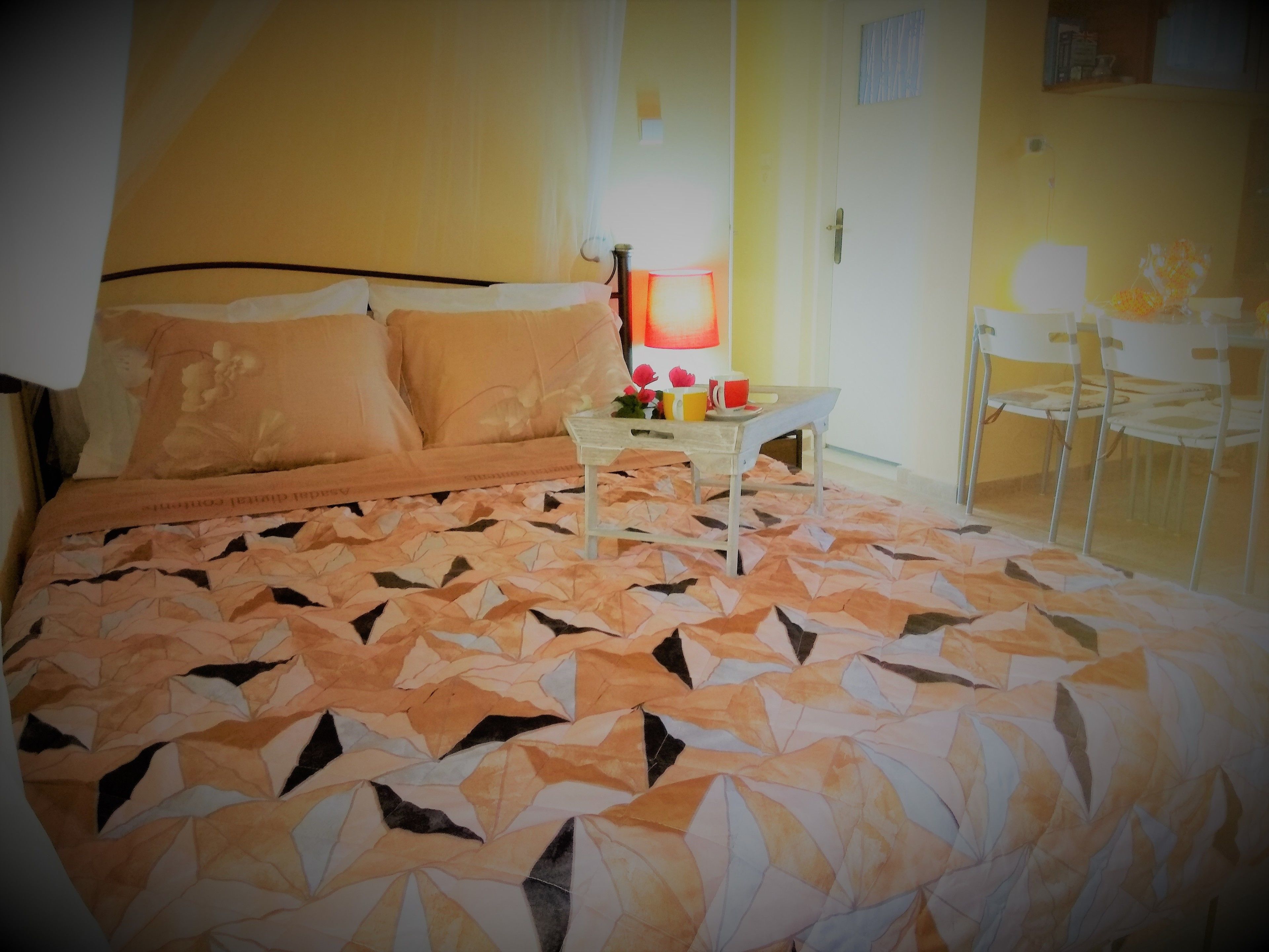 A bed with a patterned bedspread, a bedside table with a lamp, and a chair in a room with yellow walls.