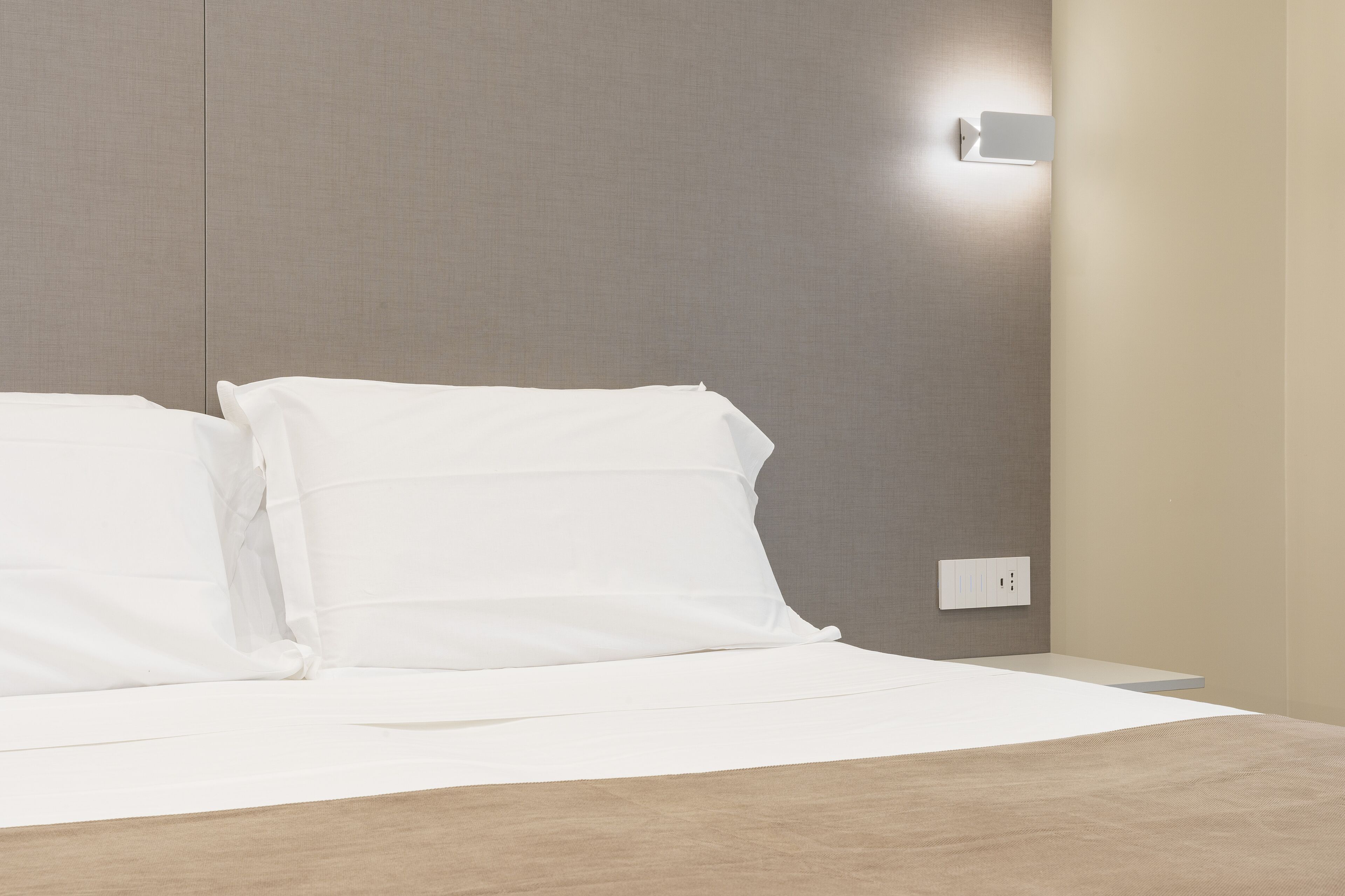 A neatly made bed with white linens in a modern hotel room.