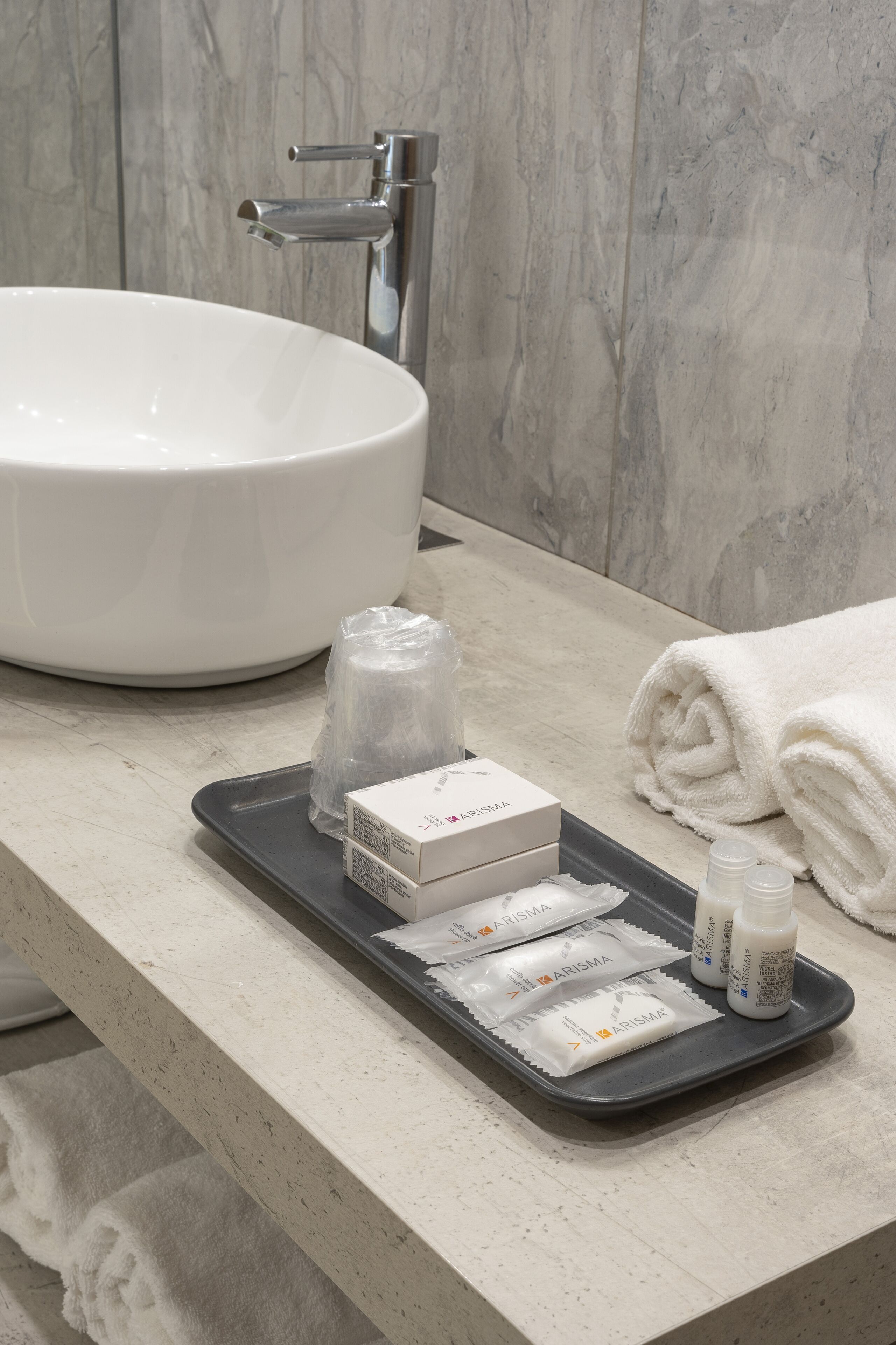 Une salle de bain avec un lavabo blanc, une serviette et des articles de toilette disposés sur un plateau.