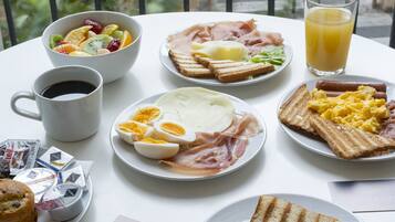 Ett frukostbord med olika sorters mat, inklusive rostat bröd, ägg, skinka och en skål med frukt.
