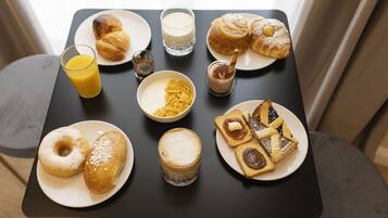 Una tavola imbandita per la colazione, con croissant, pasticcini, cereali e bevande.