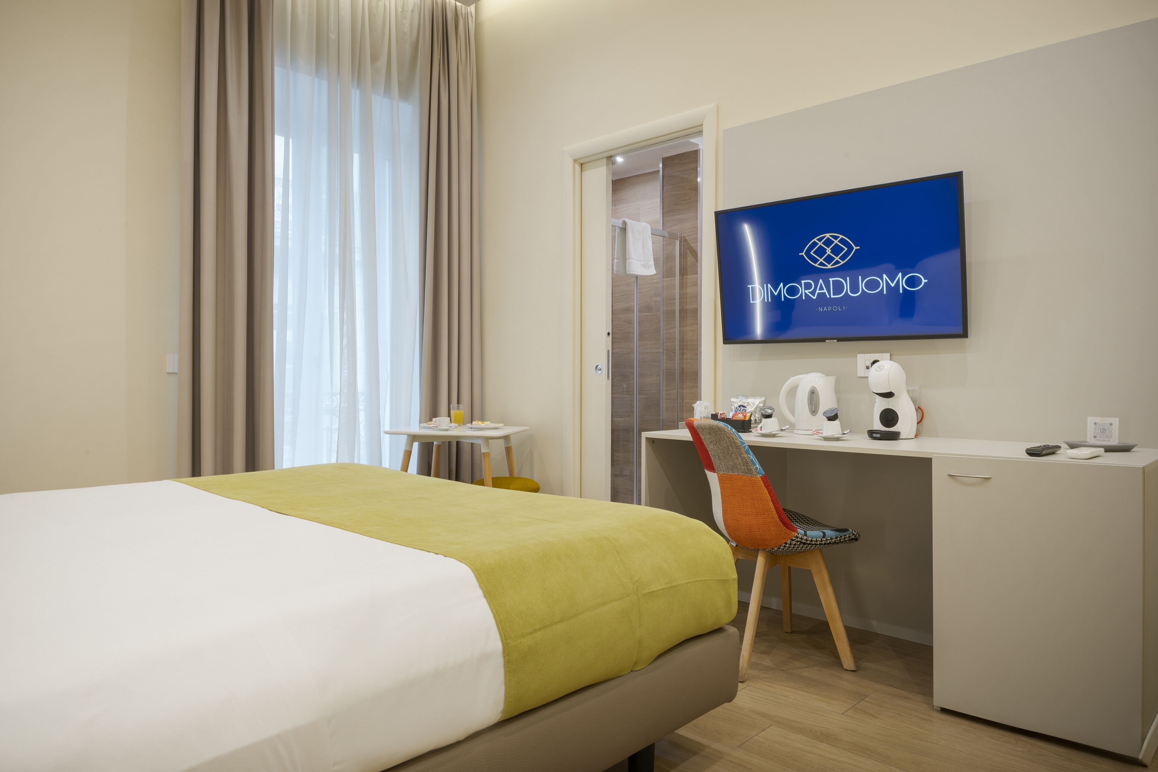 Een hotelkamer met een bed, een bureau met stoel, een televisie en een koffieapparaat.