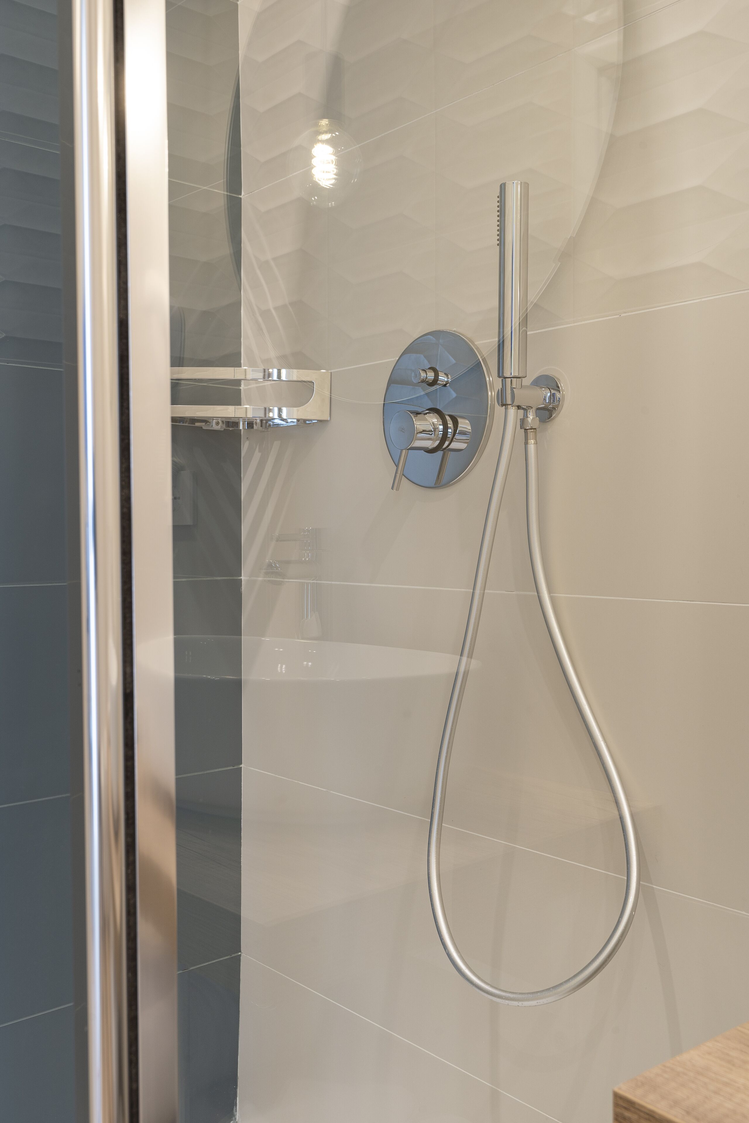Een moderne badkamer met een glazen douchecabine, een handdouche en een bedieningspaneel aan de muur.