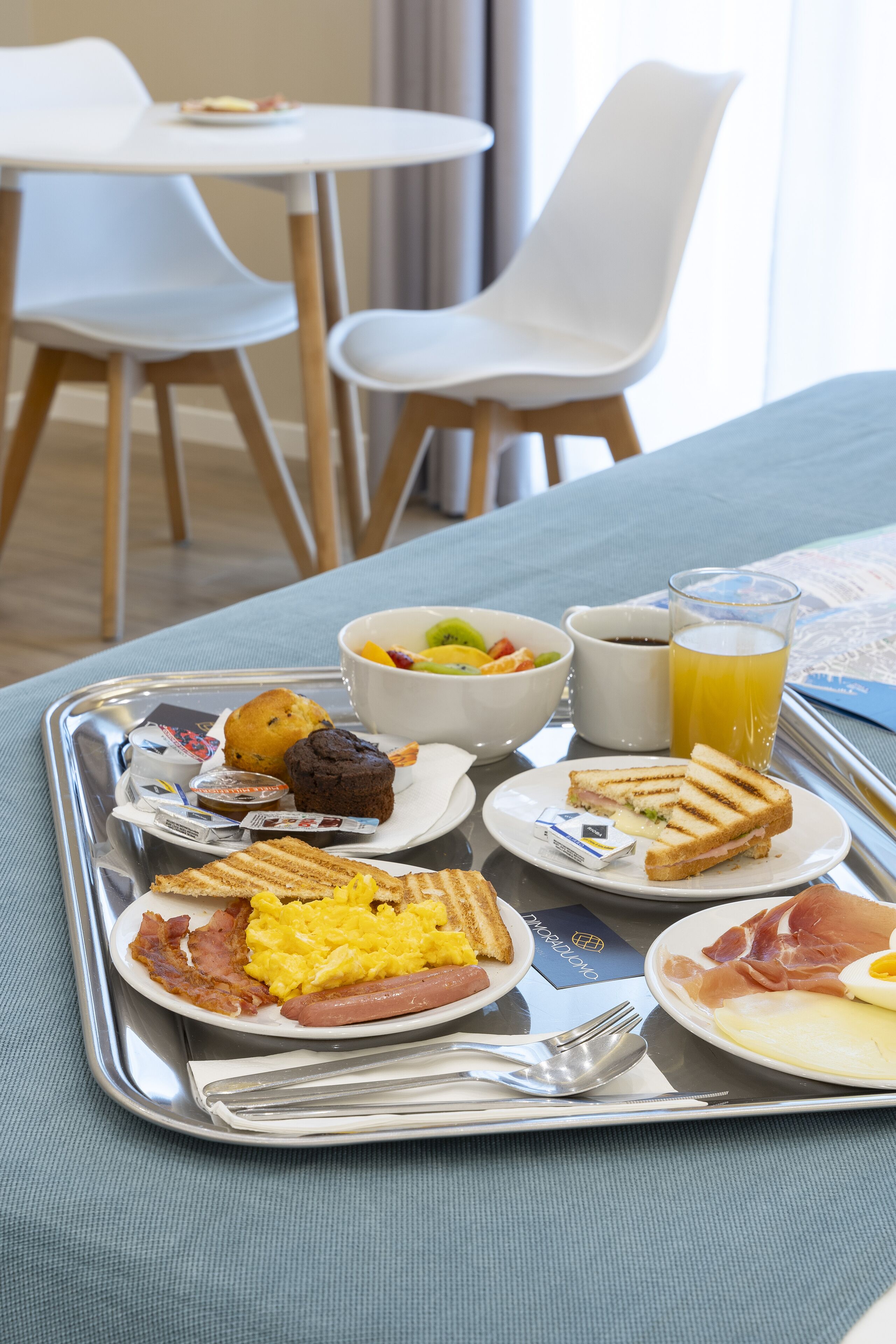 Un plateau de petit-déjeuner avec des œufs, du bacon, des saucisses, des toasts, des muffins et un saladier de fruits.