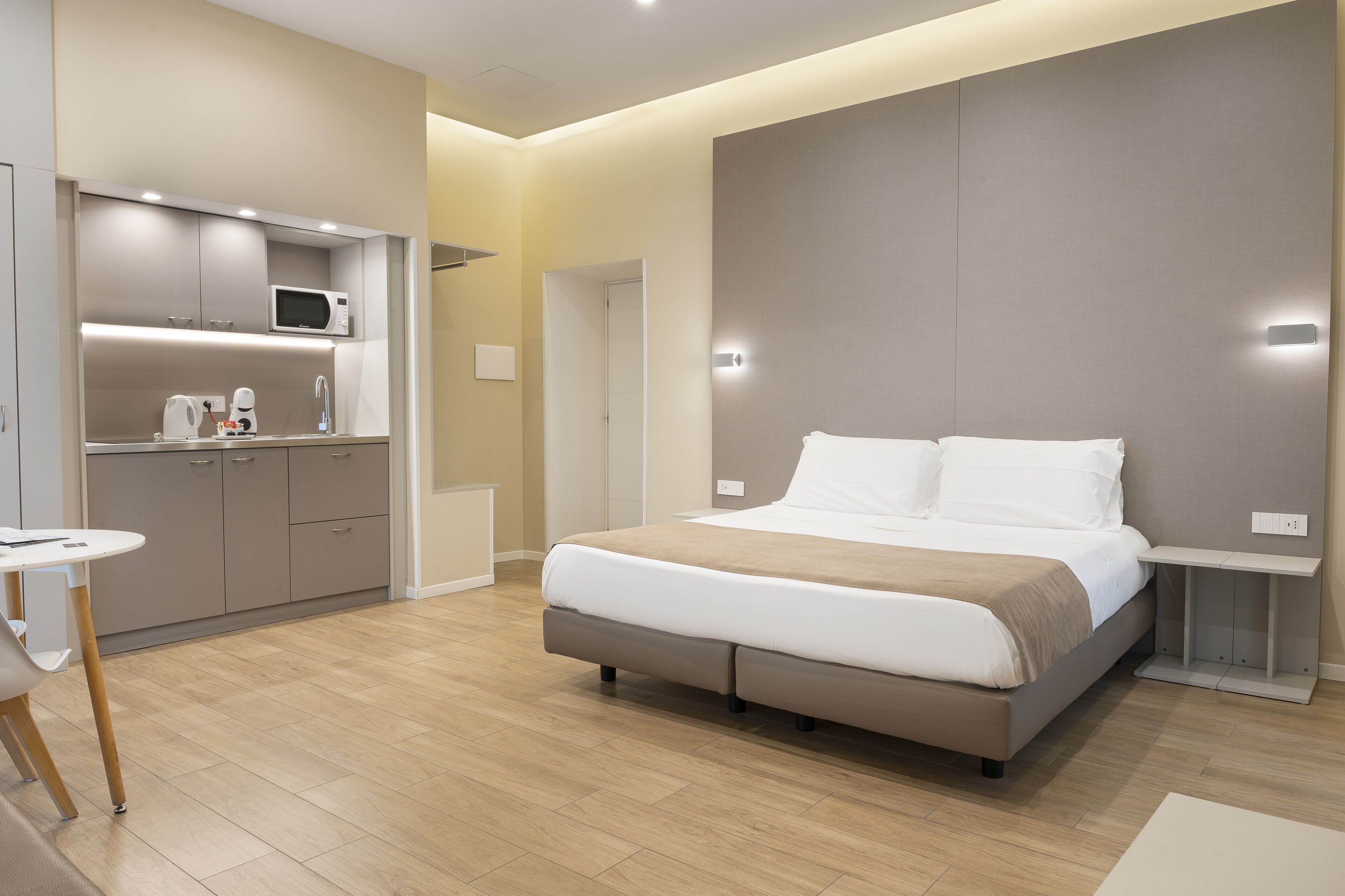 A modern hotel room with a large bed, a small kitchenette, and a separate dining area.