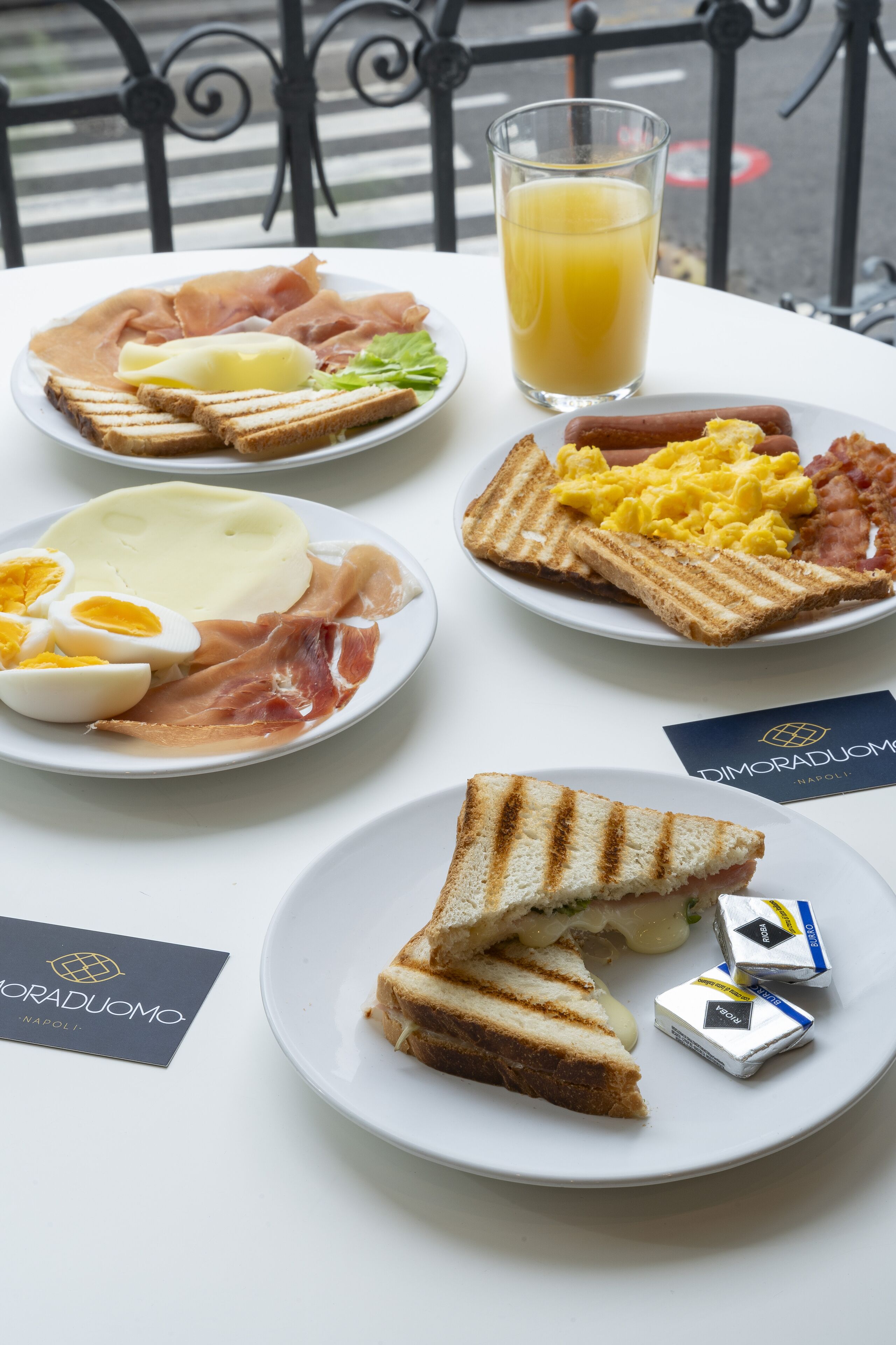 A breakfast setting with plates of toast, eggs, ham, and a glass of orange juice.