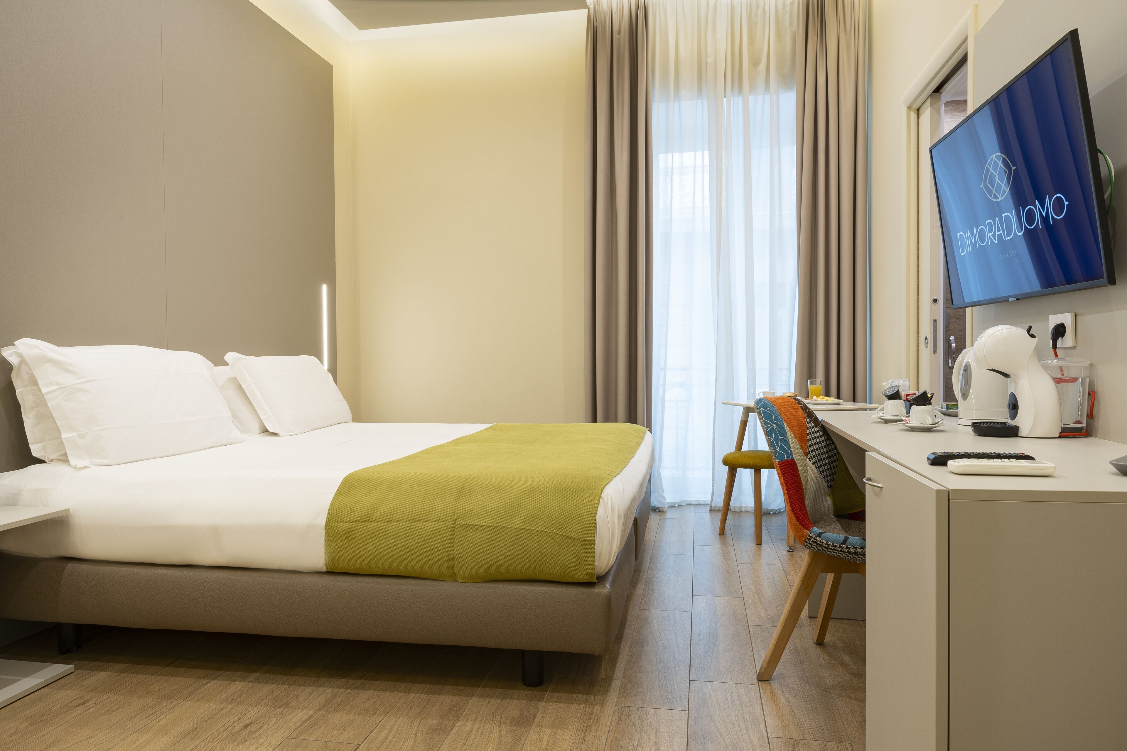 A hotel room with a bed, desk, chair, and a television displaying 'Dioradduomo'.