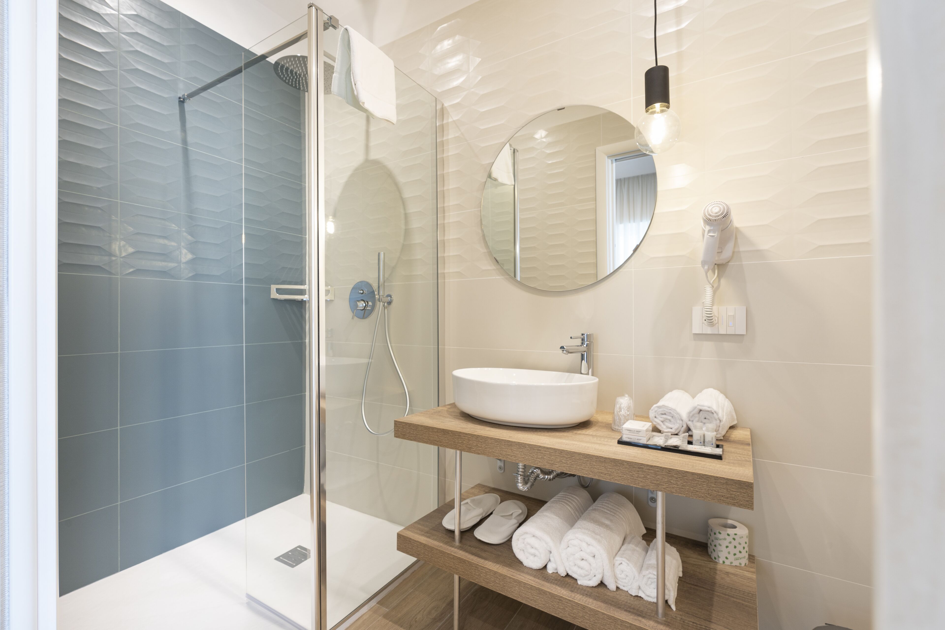 A modern bathroom with a glass-enclosed shower, a round mirror, a sink, and a towel rack.