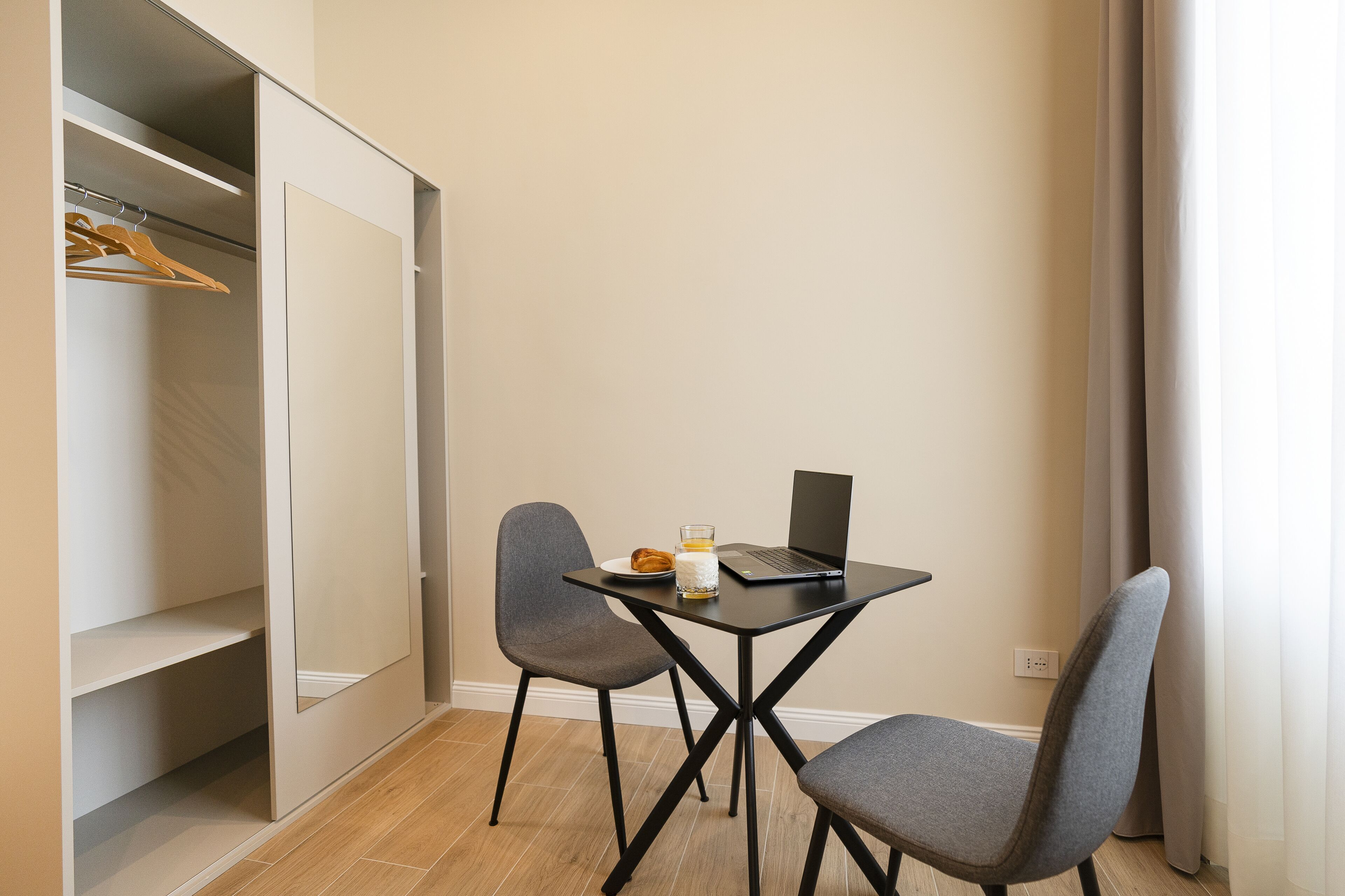 Une petite pièce avec un bureau, deux chaises, un ordinateur portable et un verre d’eau.