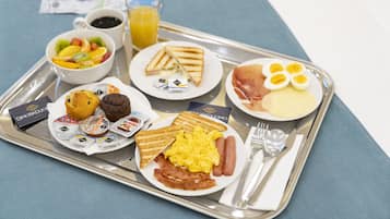 Bandeja de café da manhã com torradas, ovos, bacon, linguiça, muffins e uma saladeira de frutas.