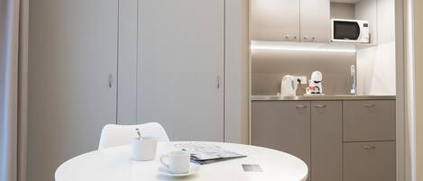 Una cocina moderna con microondas, cafetera y armarios. Hay una mesa redonda con una taza blanca y un menú.