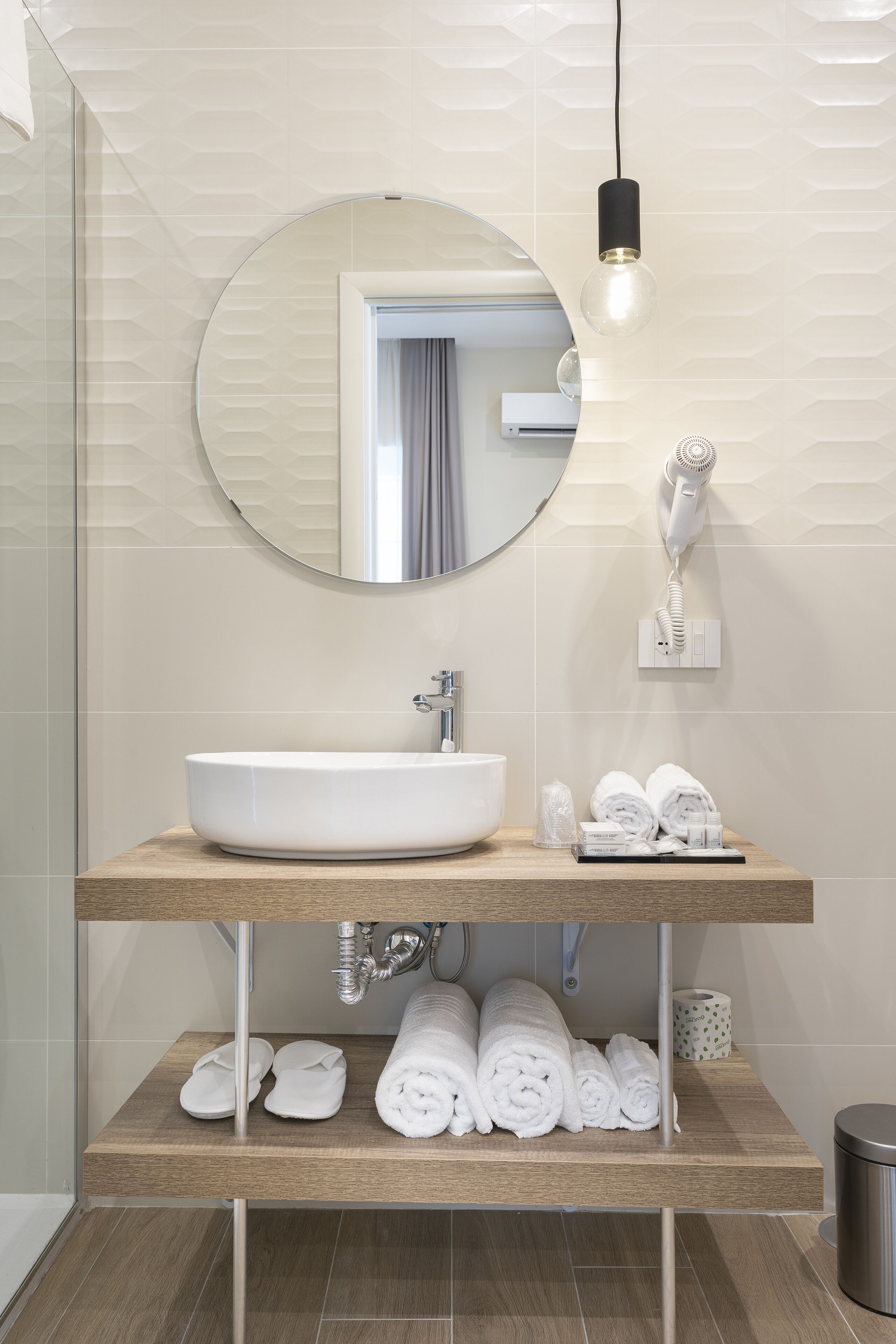 Une salle de bain moderne avec un miroir rond, un lavabo blanc et un sèche-cheveux fixé au mur.
