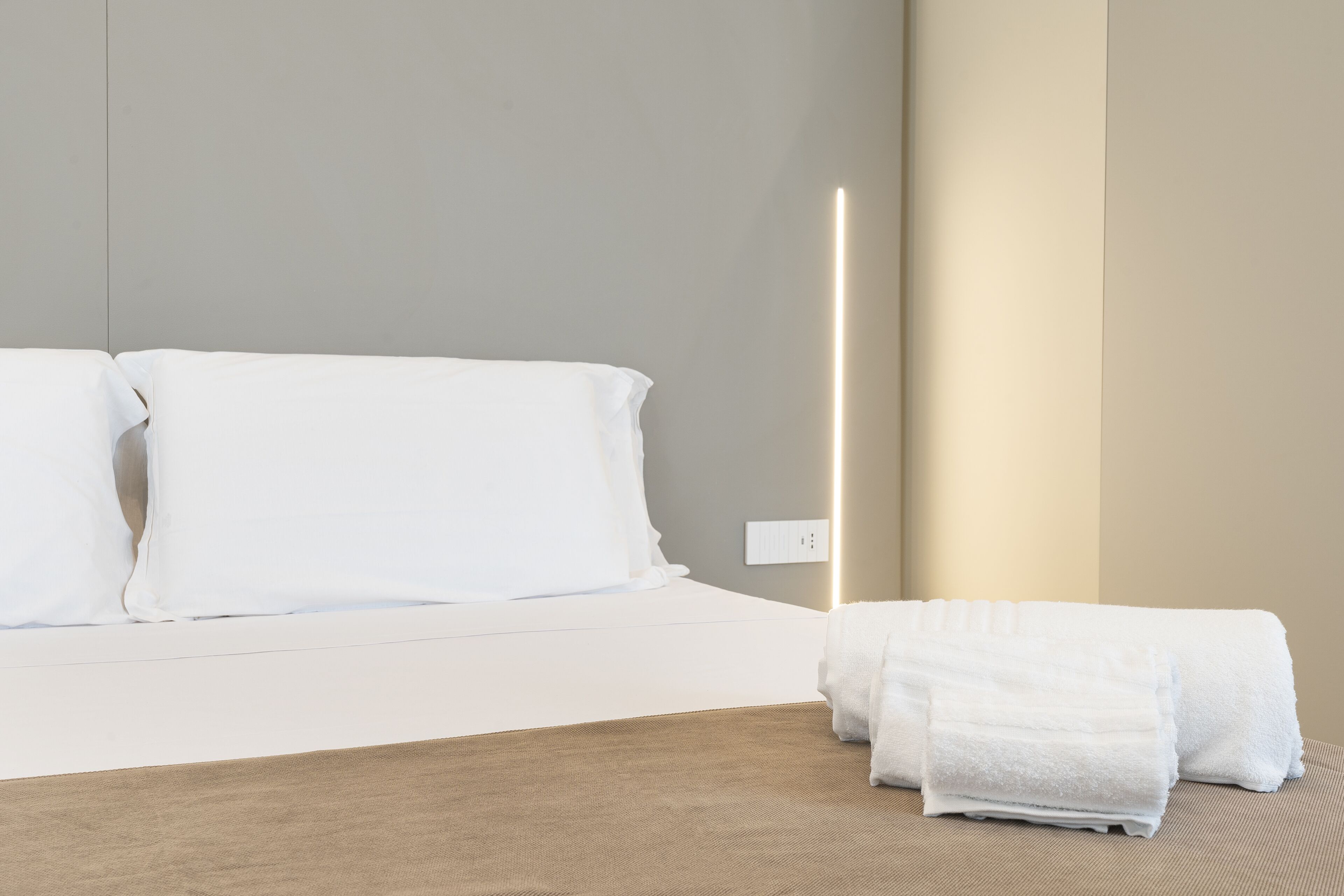 A neatly made bed with white linens and a folded white towel on the side.