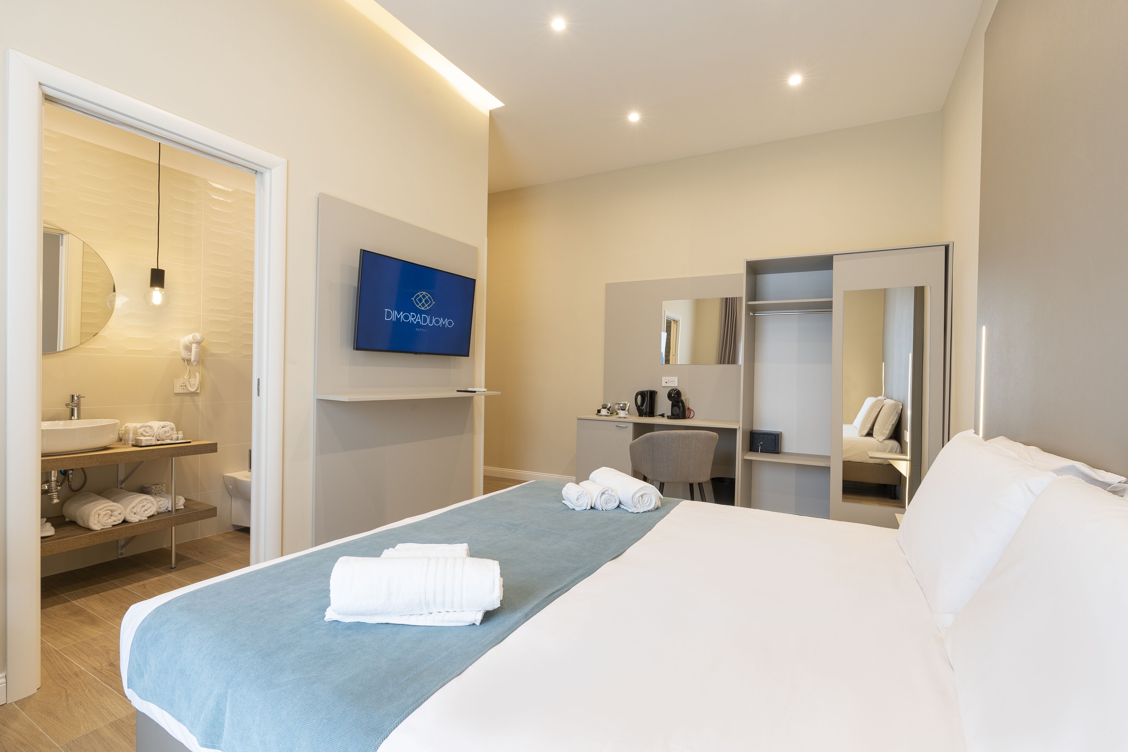 Ein modernes Hotelzimmer mit Bett, Fernseher, Schreibtisch und Badezimmer.