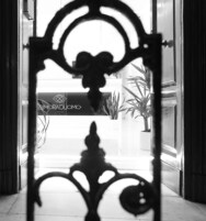 Un cancello in metallo decorato con un design simmetrico, che conduce a un ambiente interno luminoso con un cartello che indica "DIMORADUOMO NAPOLI".