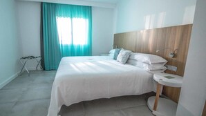 A modern hotel room with a large bed, a bedside table, a wooden headboard, and a window with curtains. - Guinate Club Apartamentos (Tías)