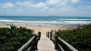 Pasarela de madera que conduce a una playa, con gente a lo lejos.