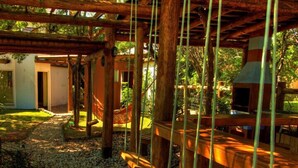 Una terraza de madera con diseño rústico, rodeada por un jardín y un edificio con chimenea.