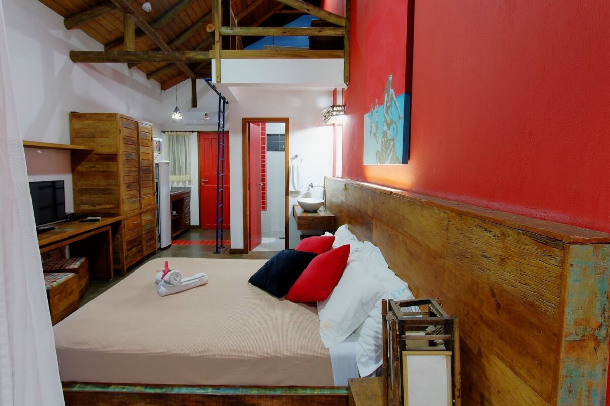 Una habitación con una cama, muebles de madera, un televisor, un escritorio y una pared roja.