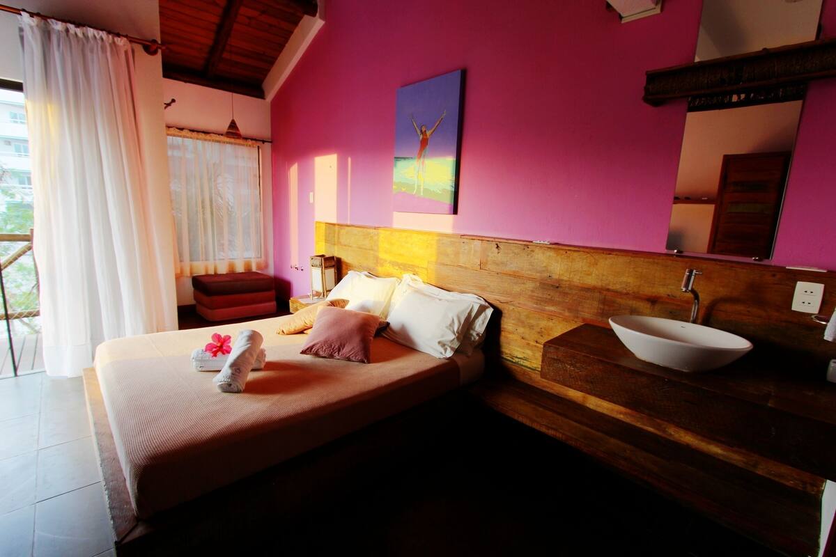Un dormitorio con cabecera de madera, una cama con almohadas, una mesita de noche con un cuenco blanco y un cuadro en la pared.