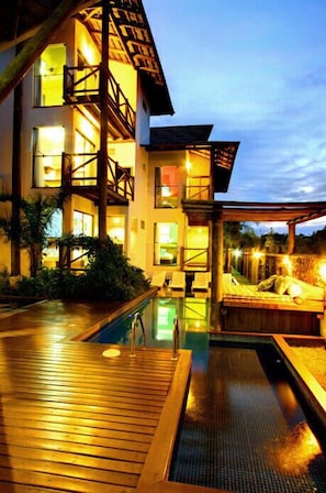 Un edificio de varios pisos con piscina, terraza de madera y mobiliario exterior.