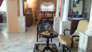 Un salón amplio con piso de mármol, una zona de comedor con mobiliario de madera y un espejo grande.