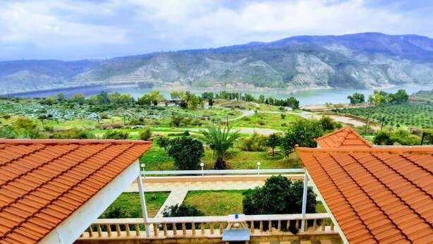 Vista de un paisaje montañoso con una masa de agua, campos en terrazas y edificios con techos de tejas rojas.