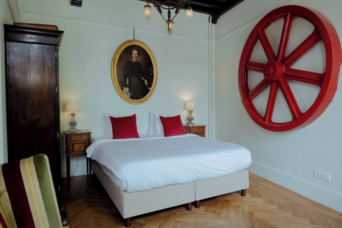 Une chambre à coucher avec un lit, une grande roue rouge, un portrait et une armoire en bois.