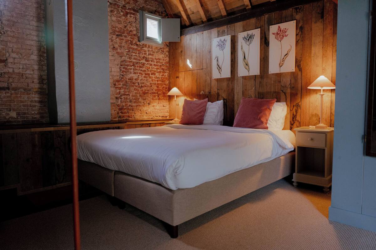 Une chambre avec un grand lit, des murs en bois, un mur en briques et des œuvres d’art encadrées.