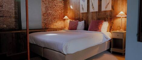 A bedroom with a large bed, wooden walls, a brick wall, and framed artwork.