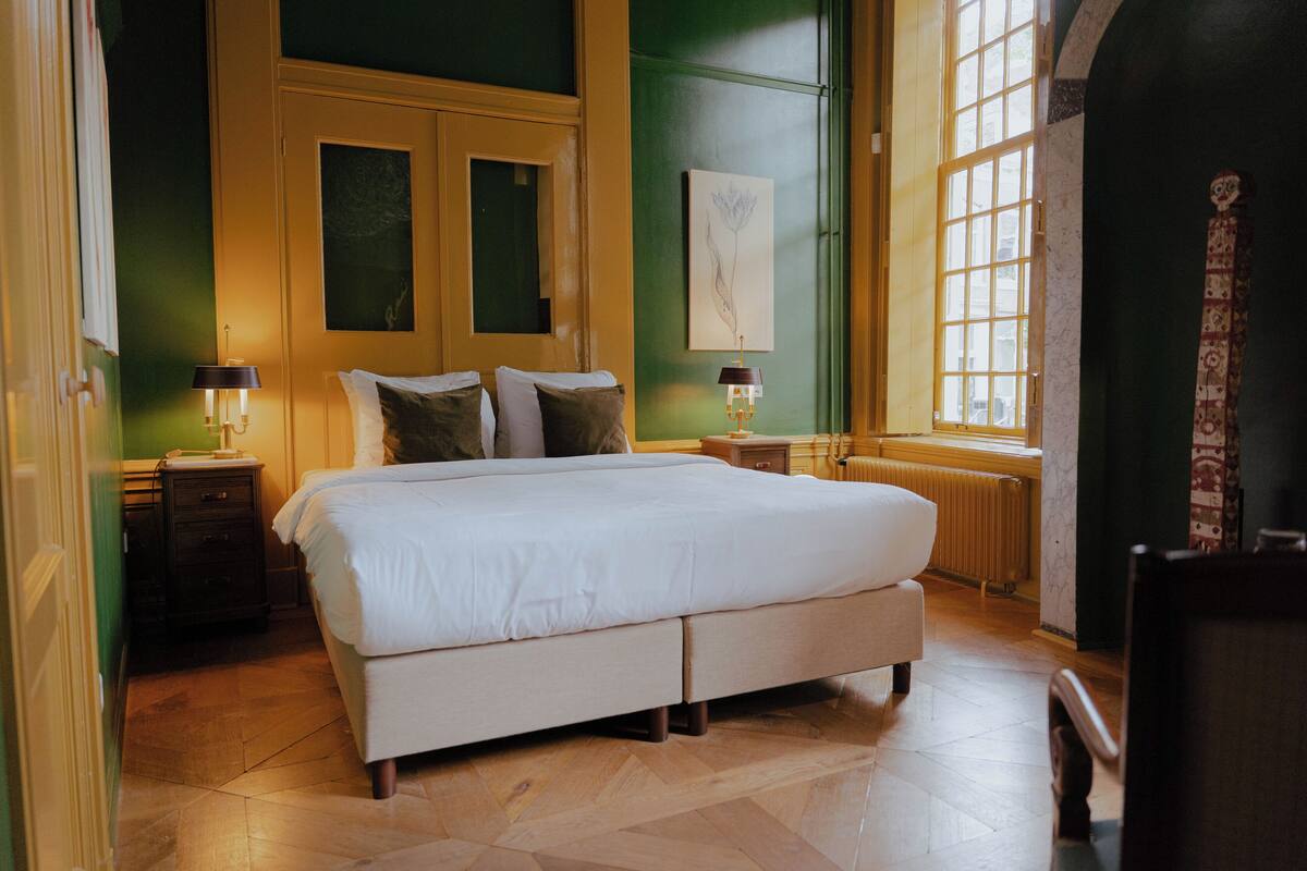Une chambre à coucher avec un grand lit, deux tables de chevet, un radiateur et une fenêtre donnant sur un beau paysage.