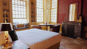 A hotel room with a large bed, a round table, and a fireplace.