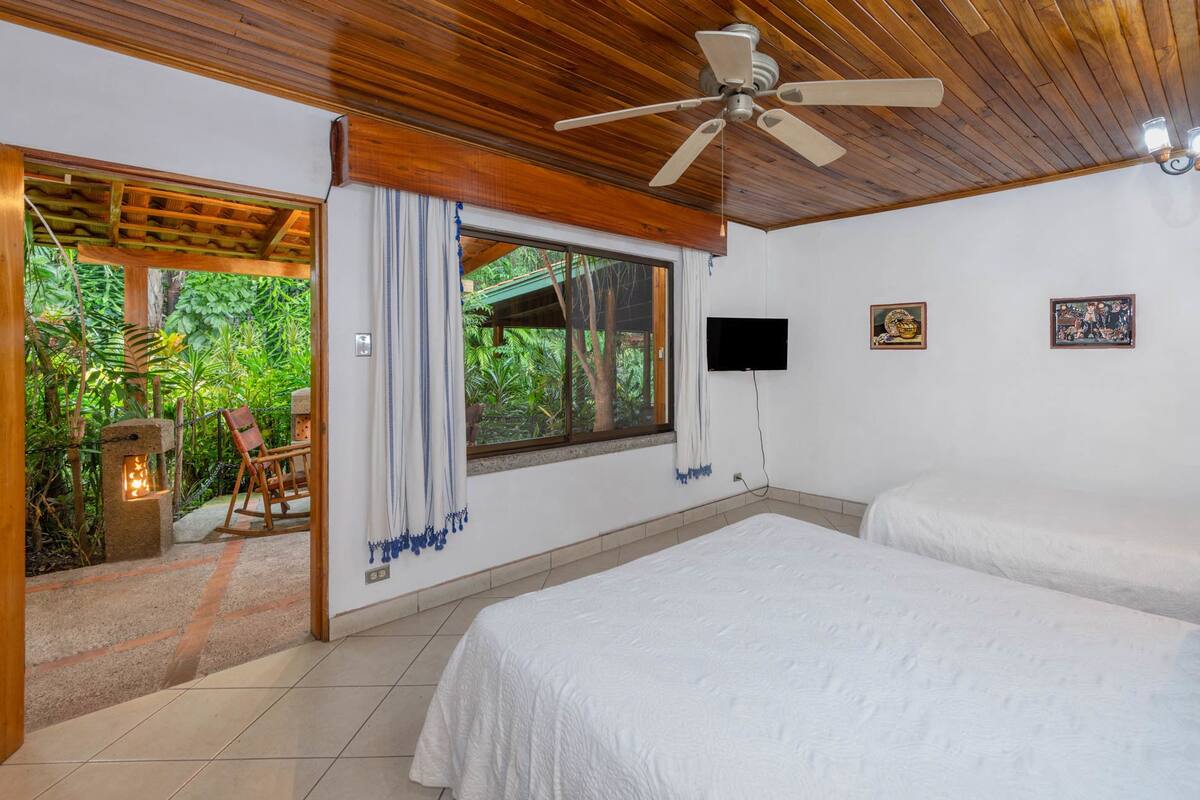 A bedroom with two beds, a ceiling fan, a TV, and a window with curtains.