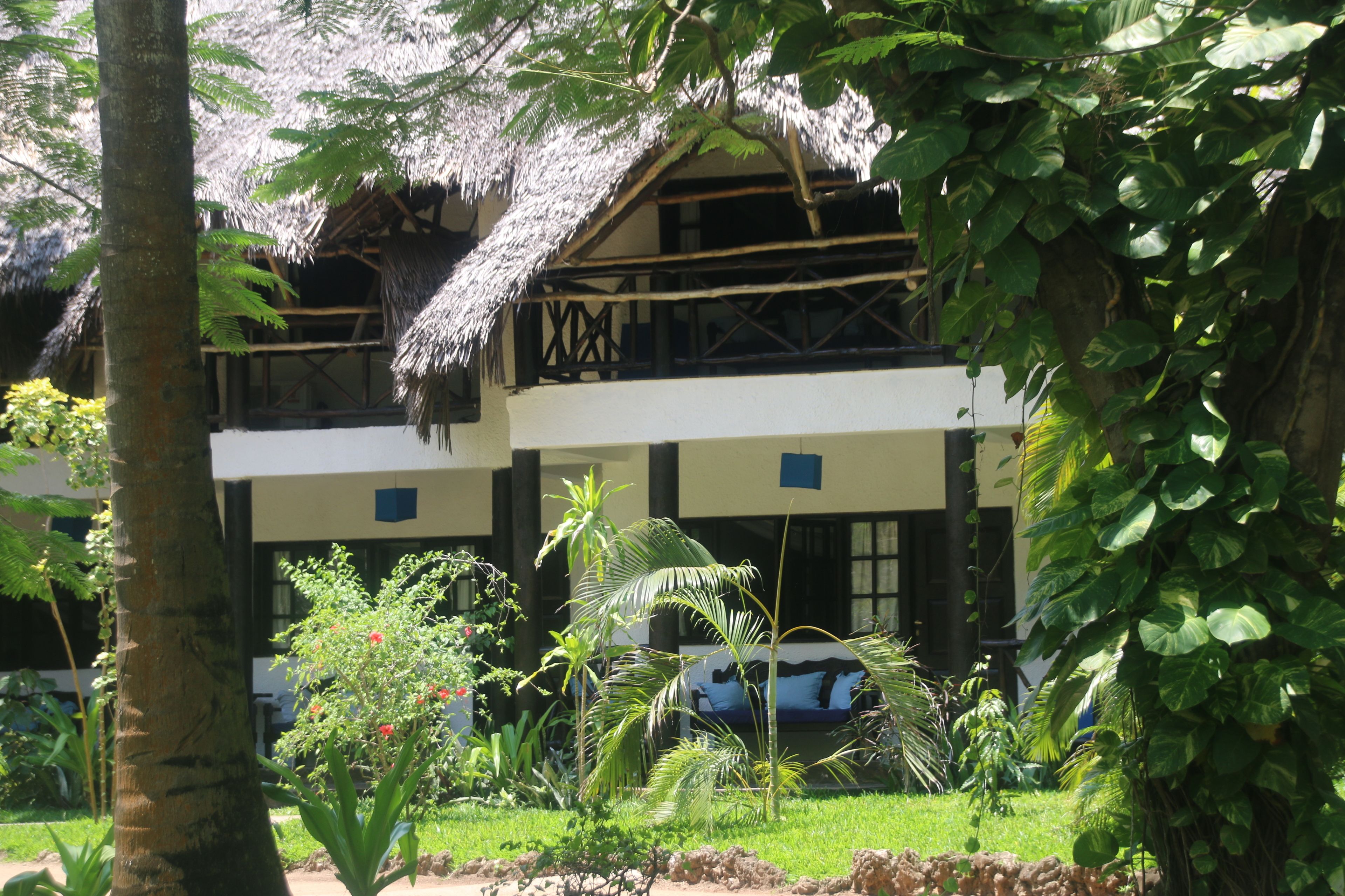 A two-story building with a thatched roof, surrounded by lush greenery and a well-maintained lawn.