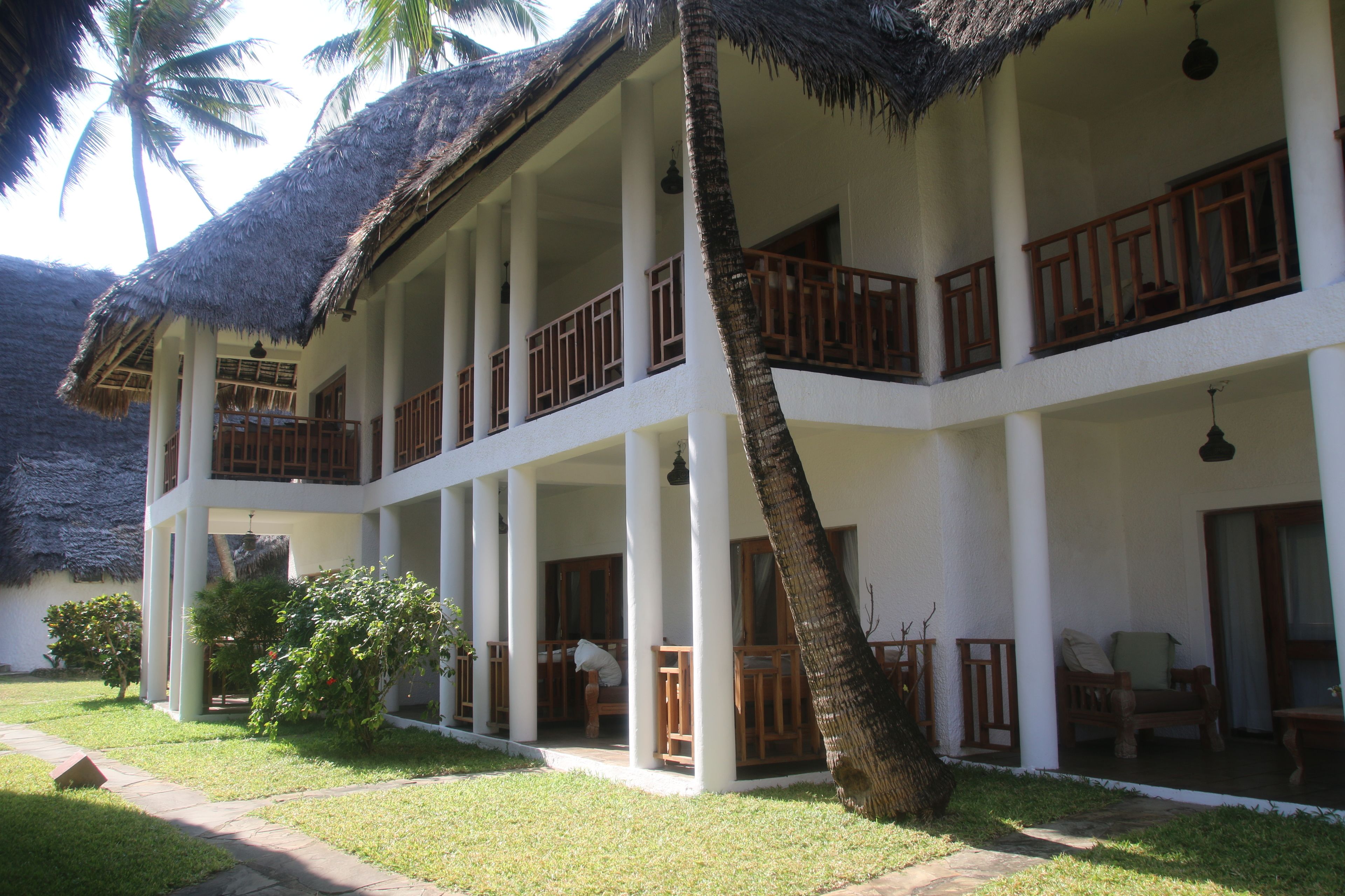 A two-story hotel with a thatched roof, multiple balconies, and a well-maintained lawn.