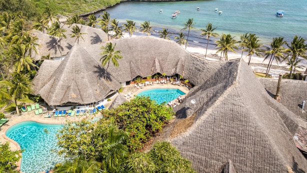 Un resort con piscina rodeada de construcciones de techo de paja, palmeras y vistas al océano.
