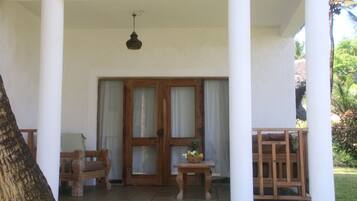 Un espacio al aire libre cubierto con un banco de madera, una mesa pequeña con una cesta y una puerta con paneles de vidrio.